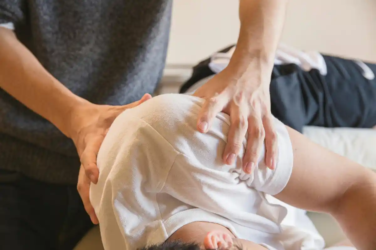 A chiropractor or physical therapist is performing an adjustment on a patient, gently manipulating their back and shoulder while they lie on a treatment table.