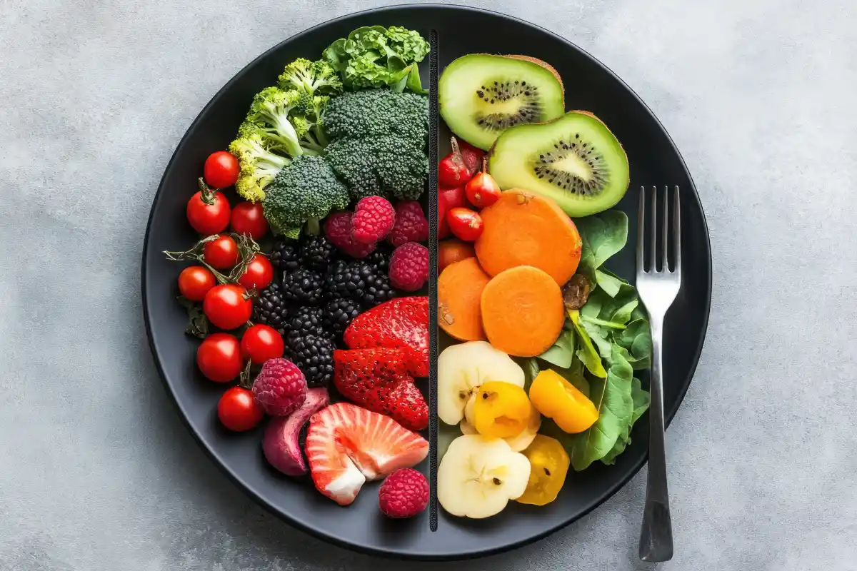 A healthy plate divided into two sections, one with fresh vegetables like broccoli, tomatoes, and carrots, and the other with colorful fruits such as strawberries, kiwis, and berries. A fork is placed next to the plate.