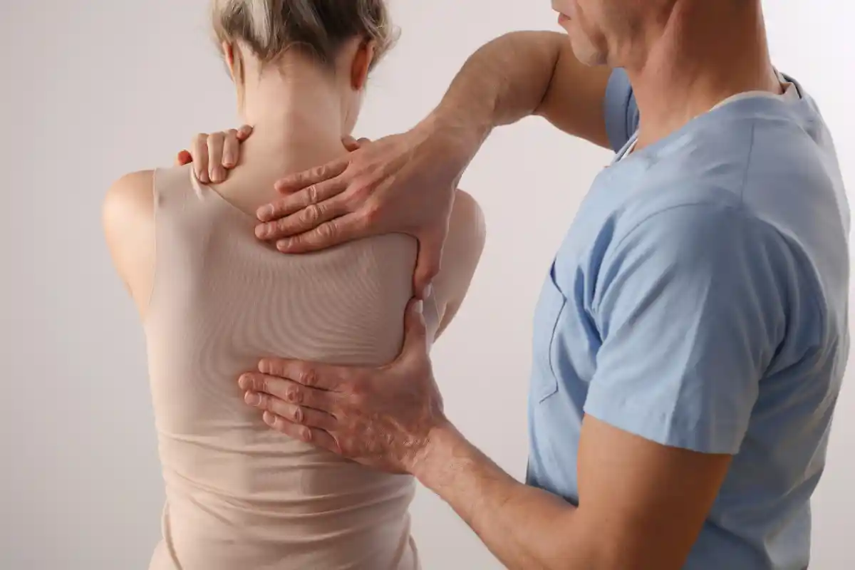 A chiropractor or therapist is providing a back adjustment to a patient, using their hands to gently support and manipulate the patient's upper back.